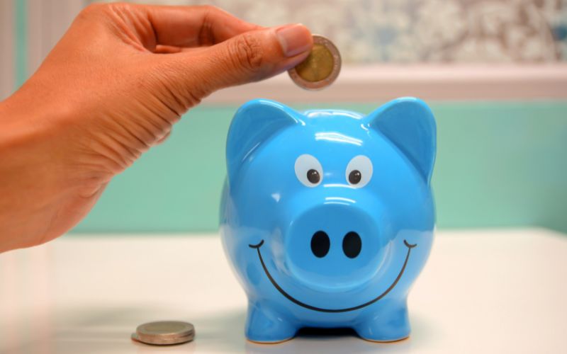 Ein blaues Sparschwein wird mit einer Euro-Münze gefüttert.