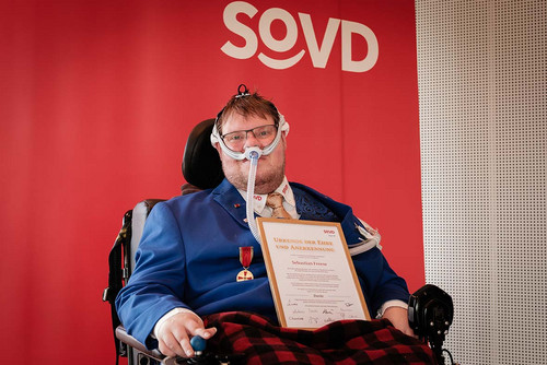 Junger Mann in einem Rollstuhl mit einer Urkunde auf dem Schoß. 