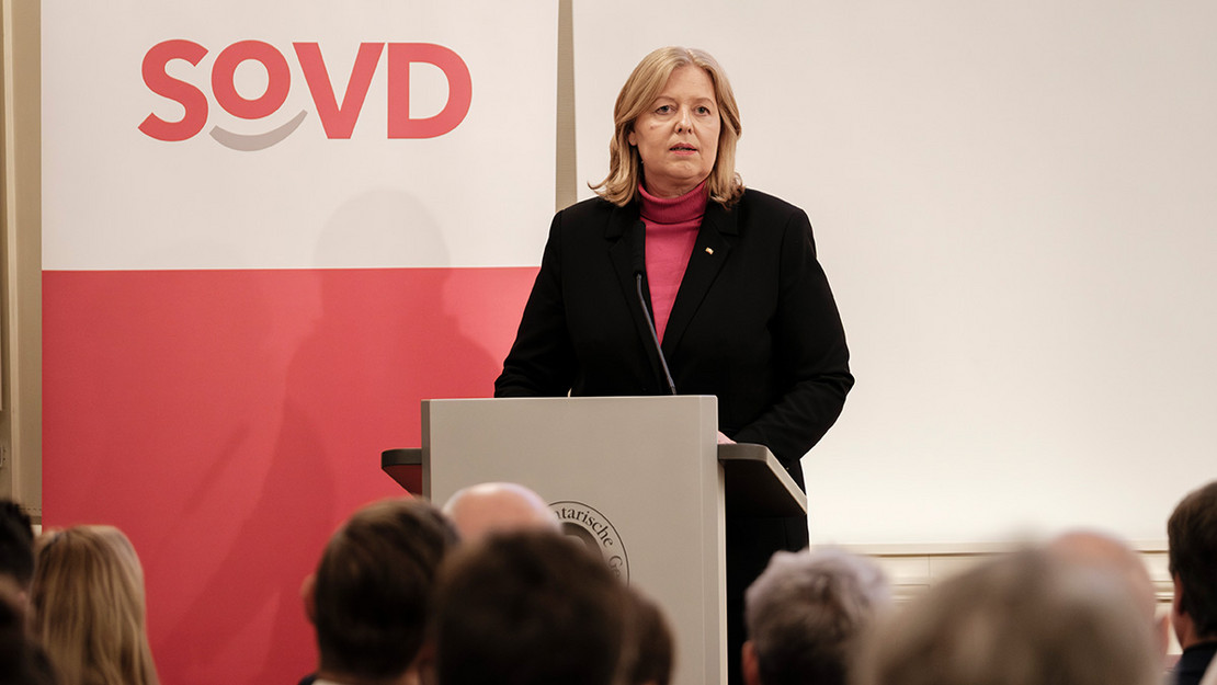 Frau steht an einem Pult und blickt auf das Publikum. 