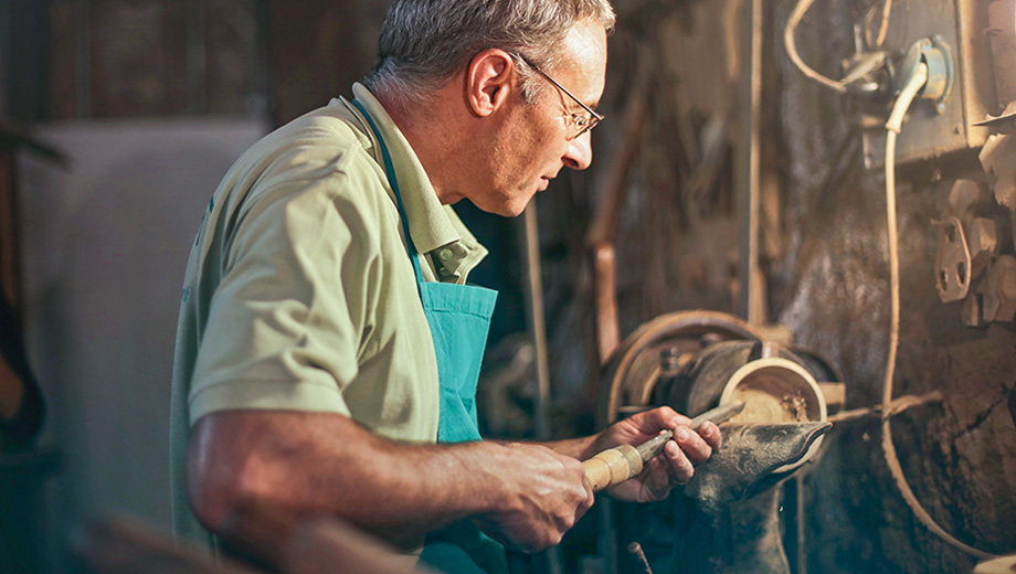 Älterer Drechsler, der in der Werkstatt an der Drechselmaschine arbeitet.